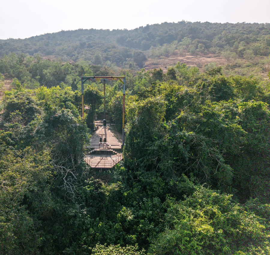 A view looking down at a tall metal structure hidden amongst green trees.