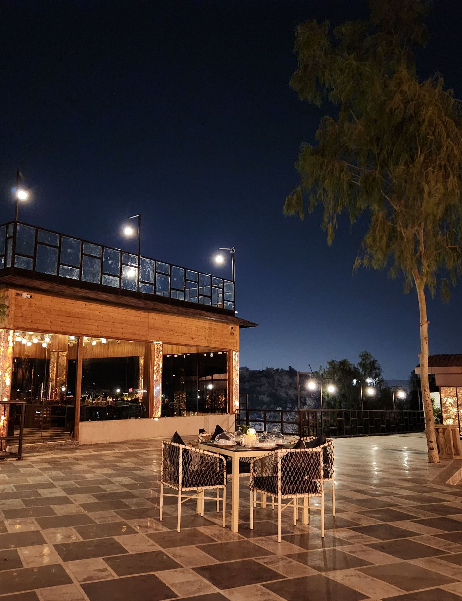 An outdoor dining area at night with a table and chairs set on a paved patio. - Bamboo Saa Resort & Spa, Udaipur
