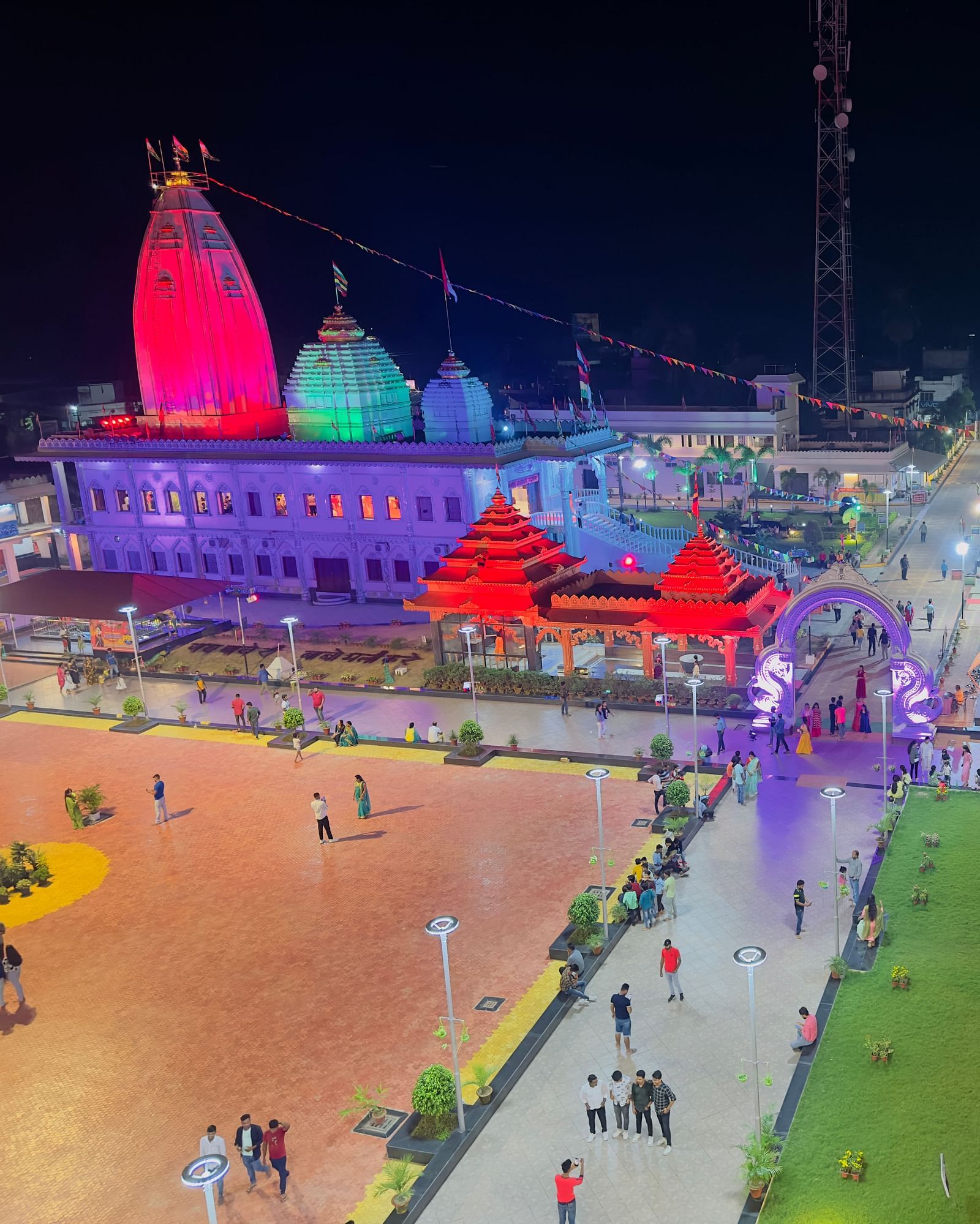 An elevated night view captures a brightly illuminated temple complex with colourful lights and pathways.