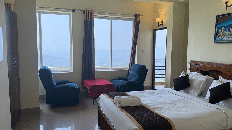 A bedroom showing a double bed with white linen, blue armchairs by the window, and a door leading to a balcony | Kollanoor Guest House, Coorg