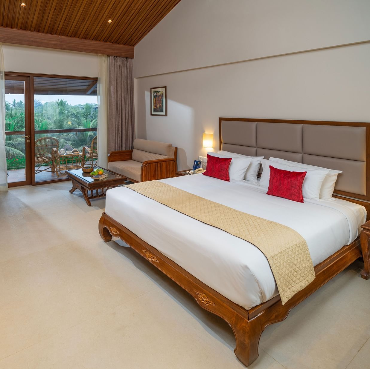 Exotica Room at Uday Suites with wooden furniture, plush bedding, warm lighting, balcony seating, and lush greenery views for a relaxing stay