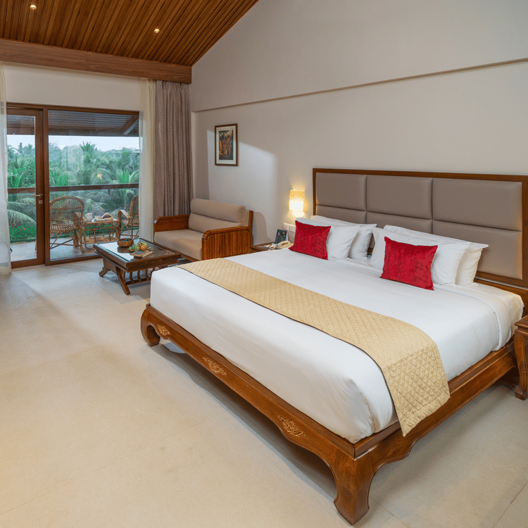 Exotica Room at Uday Suites with wooden furniture, plush bedding, warm lighting, balcony seating, and lush greenery views for a relaxing stay