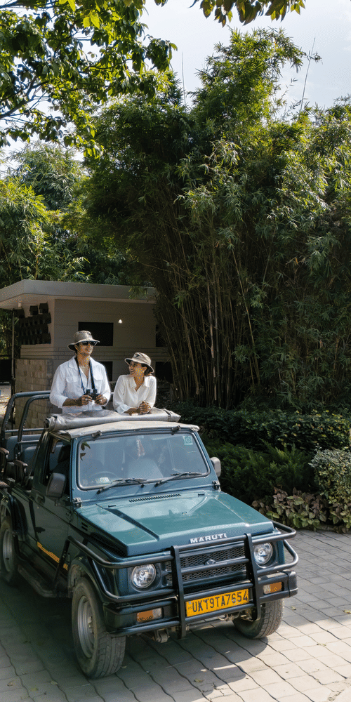 An open vehicle driving along a paved path with people seated inside and greenery on both sides.