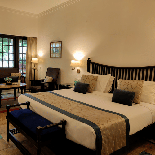 A bedroom at Jehan Numa Palace featuring a large bed with a patterned runner, warm wall-mounted lamps, and a seating area near a large window.