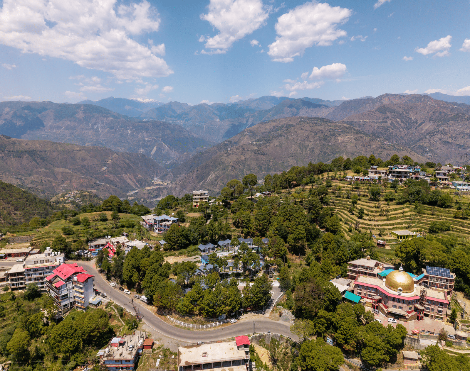 An aerial view of rolling hills, with residential and commercial buildings among lush greenery - DLS Nature Trinket Resort, best location to stay in Dalhousie.