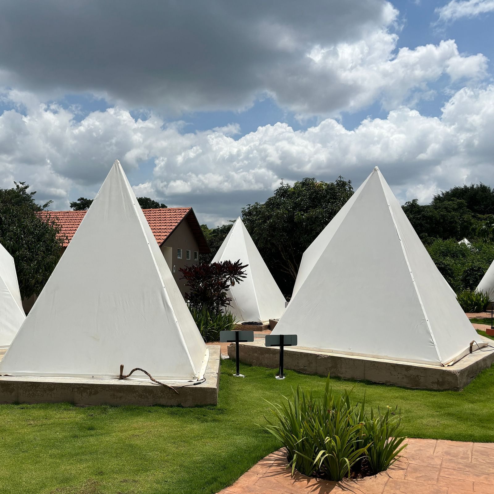 A scenic view of a resort area with tents lined along a neat walkway, surrounded by a well-maintained lawn.
