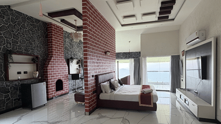 Spacious room featuring a cosy bed, fireplace, and large windows with scenic hill views.