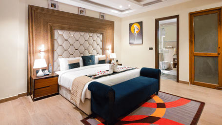 A wide angle shot of the bedroom at the Empress Suite featuring a plush double bed along with a rug on the floor in front of it at The Meriton.