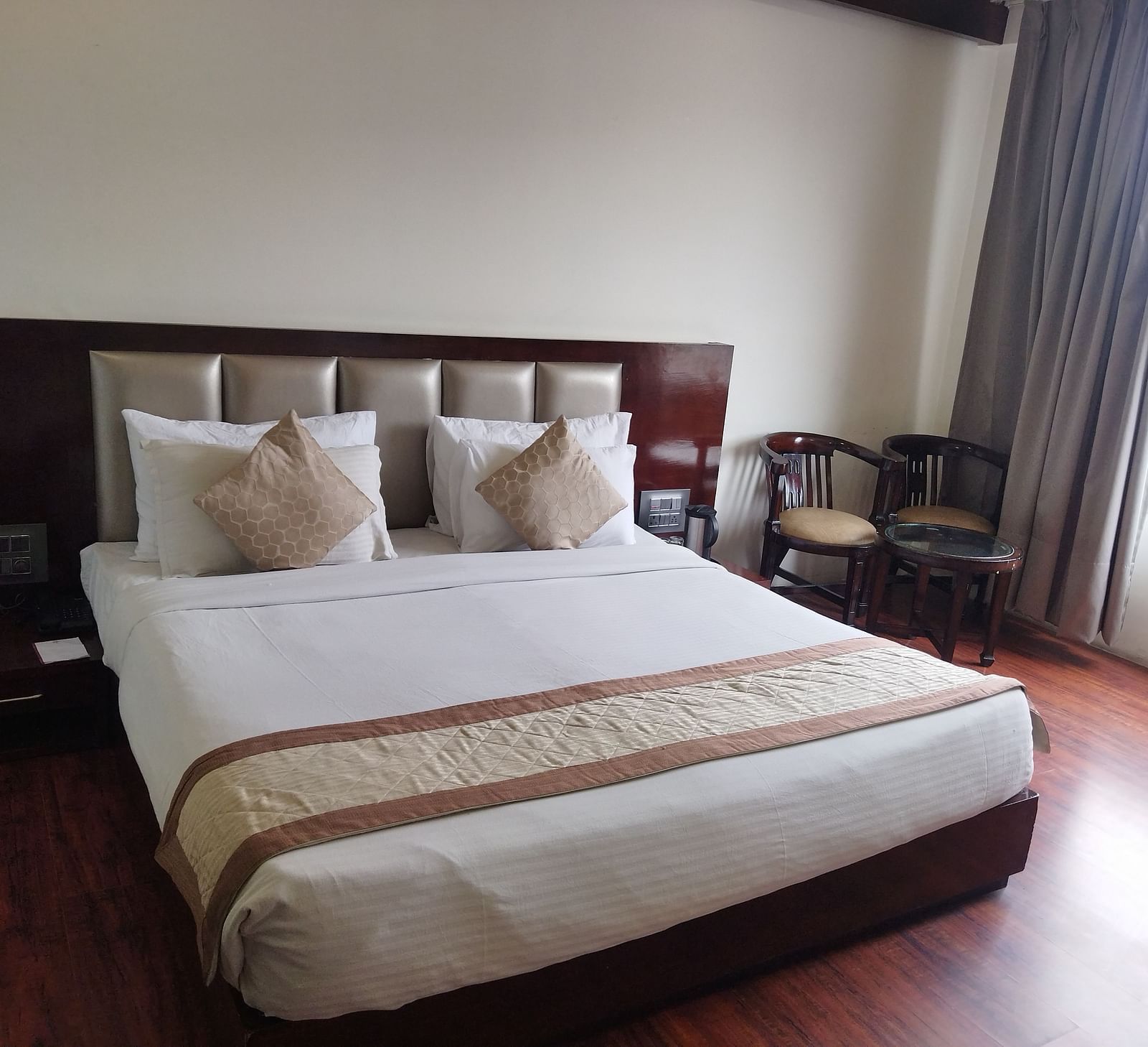 A hotel room with a large bed draped in beige and brown linens and furniture to relax - TGI Apple Inn, Jaipur 