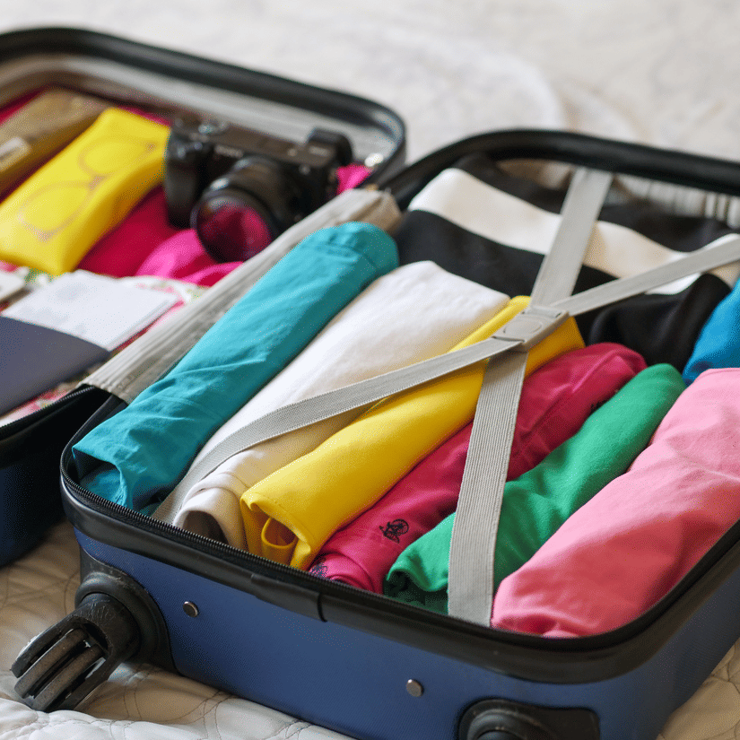 Open suitcase neatly packed with colorful clothes, travel documents, toiletries, and a camera, ready for a journey.