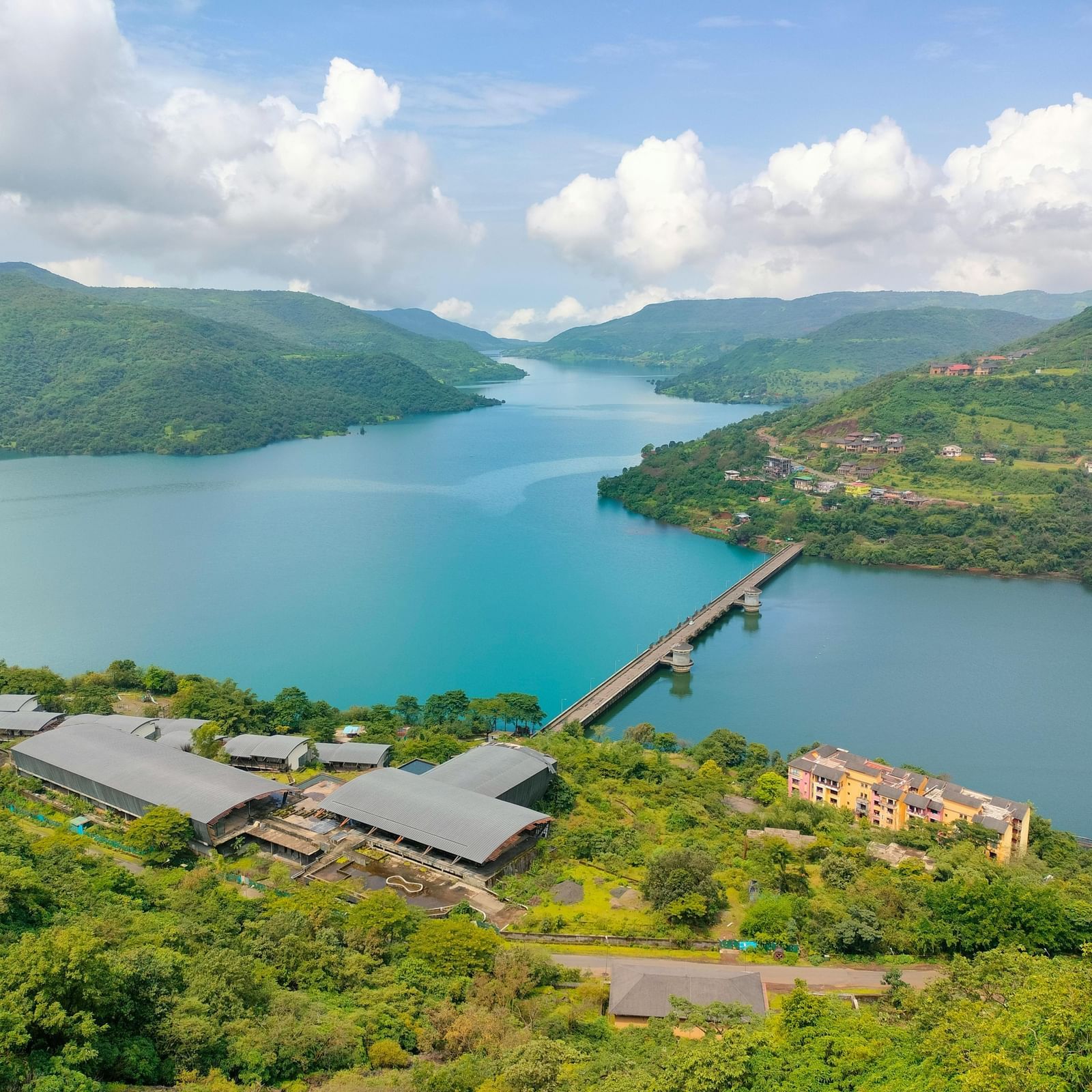 A dam stretches across a river with hills surrounding it, showing a scenic landscape and water body in a natural setting.