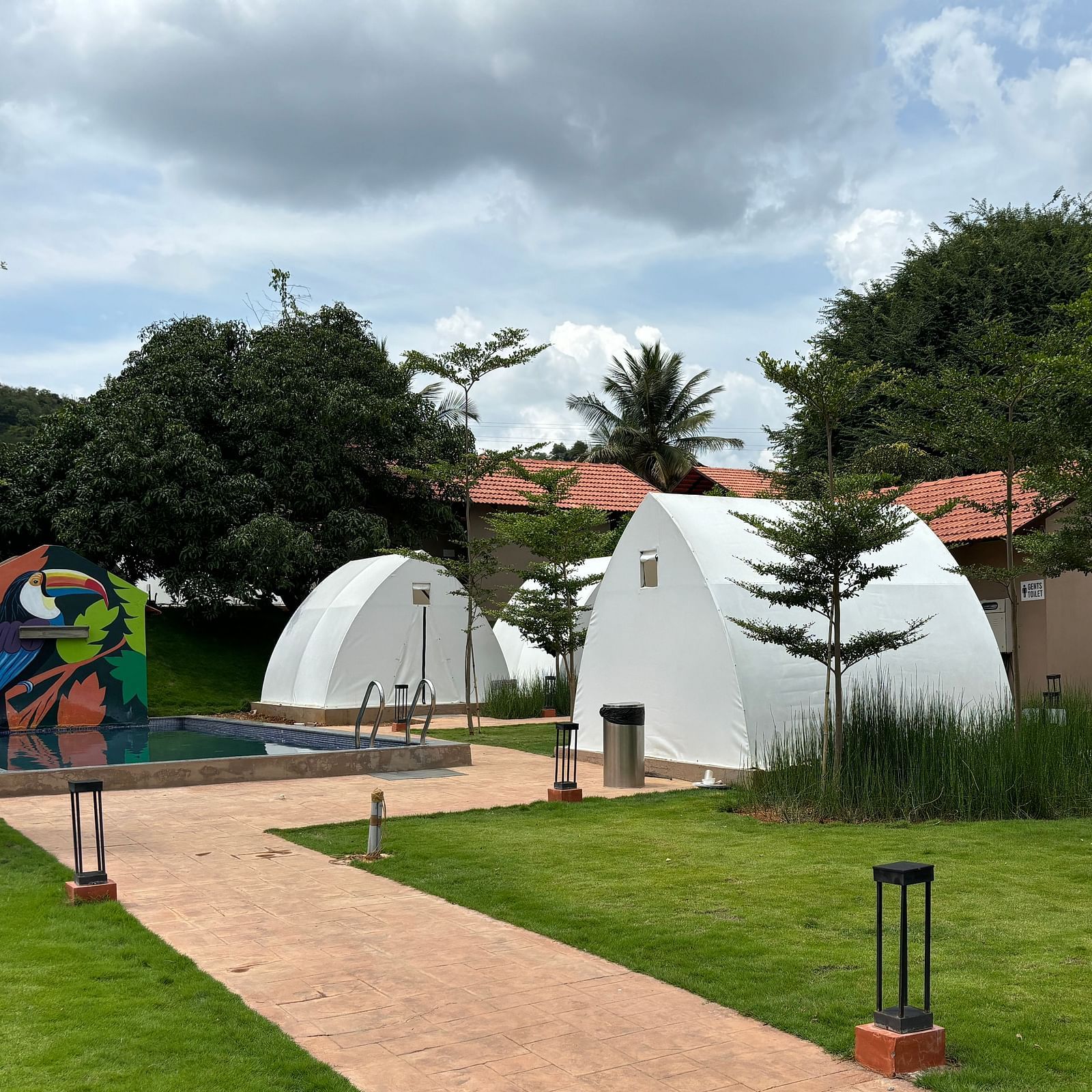 A scenic view of a resort area with tents lined along a neat walkway, surrounded by a well-maintained lawn.