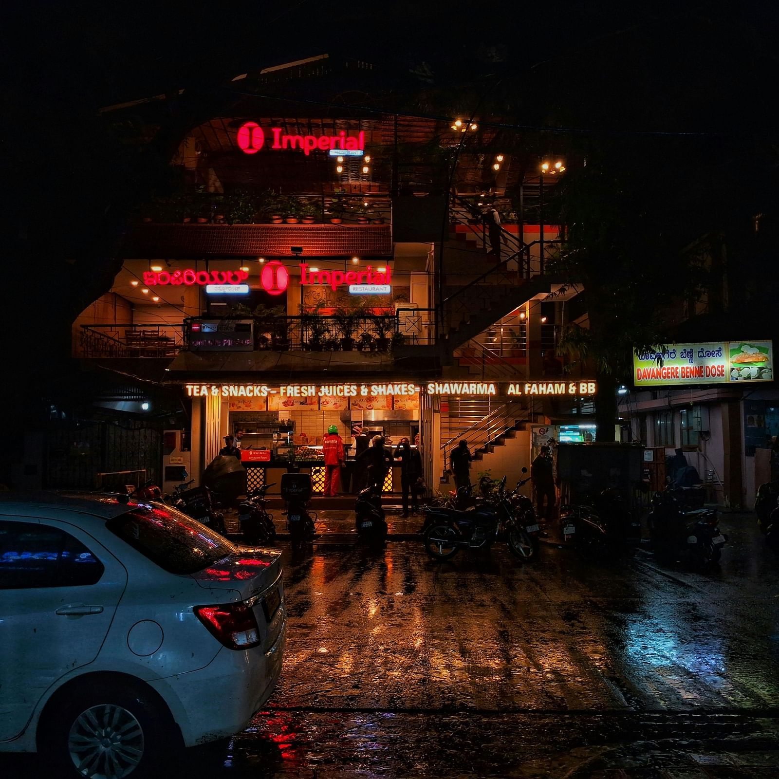 Nighttime view of a restaurant with warm lighting and a wet, reflective street.