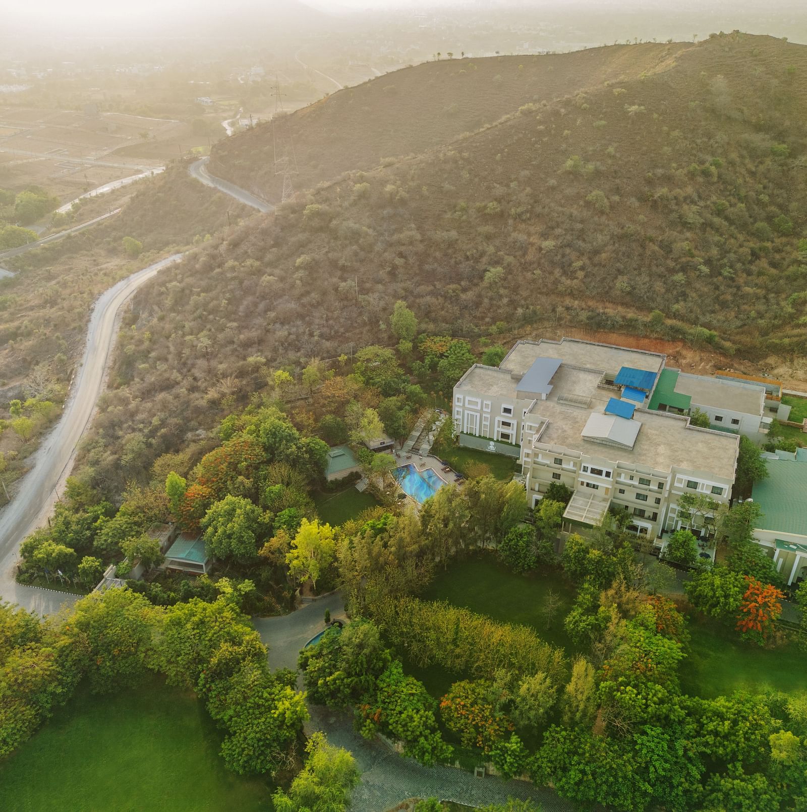 Aerial view of Essentia Luxury Resort & Spa, Udaipur with a small road and trees in view