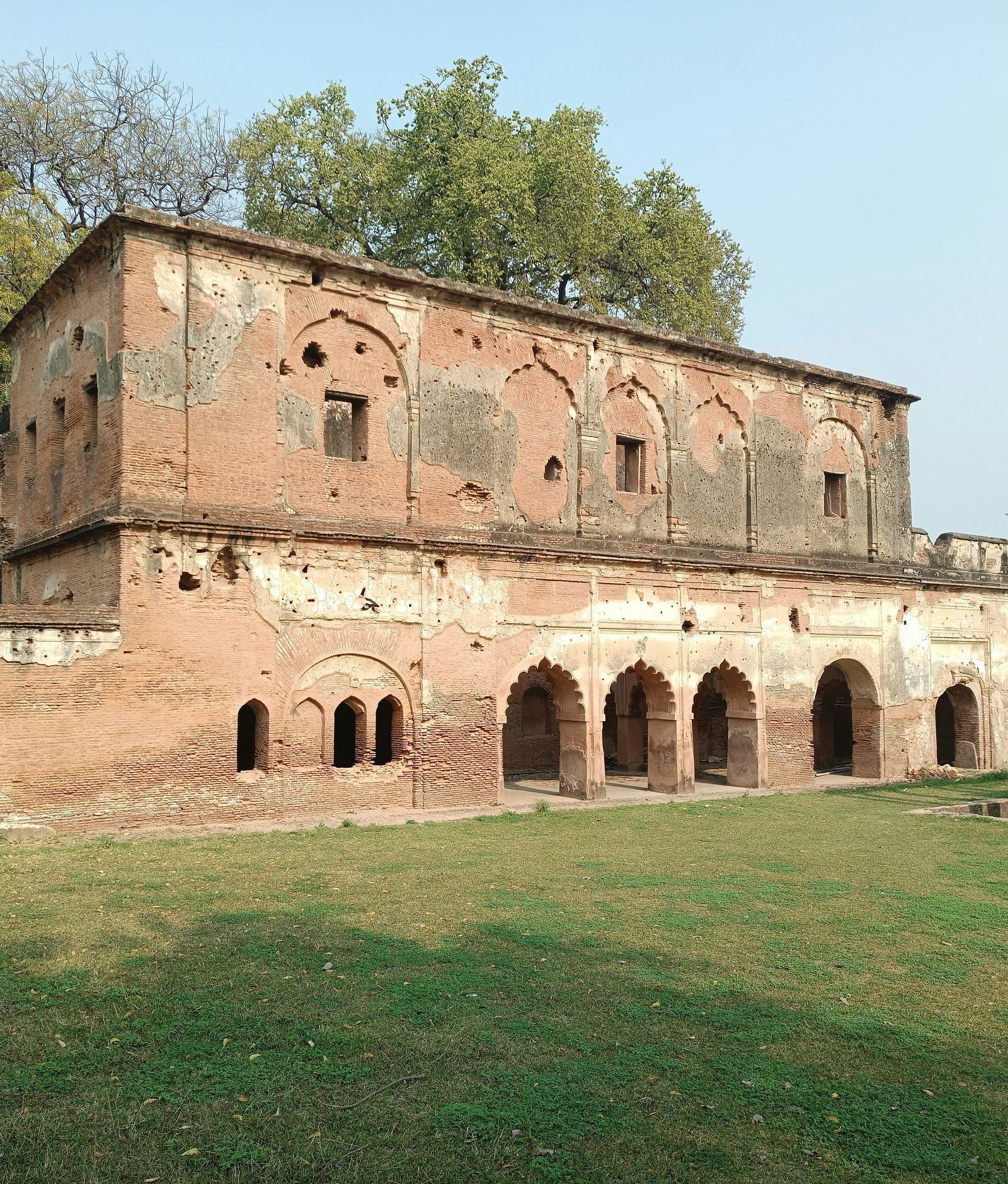 An old red stone building stands against a clear sky, with a trees in the background