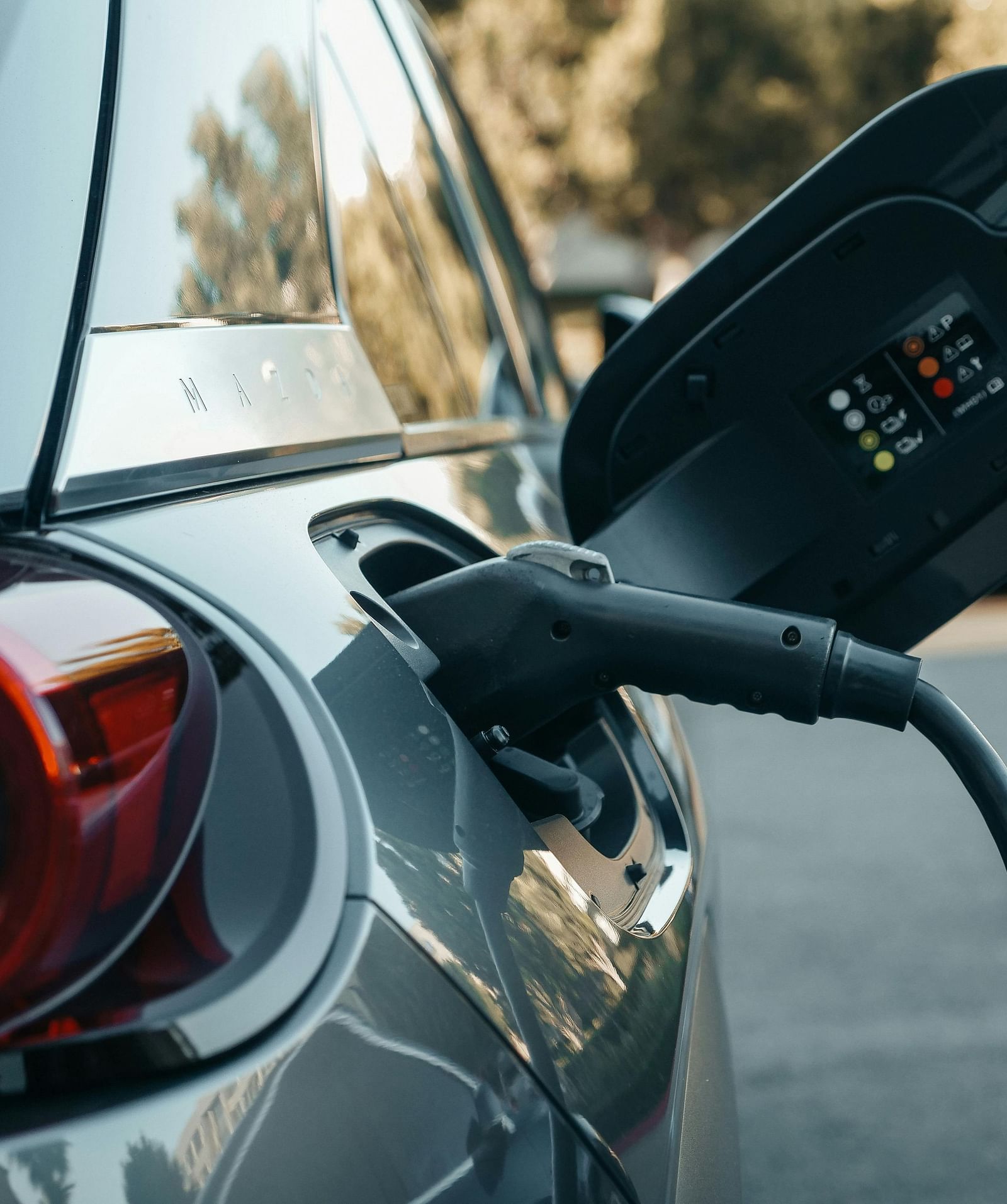 A close-up view of the rear of a silver electric car with a charging cable plugged into its charging port.