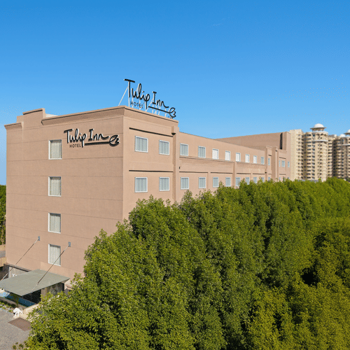 The facade of a hotel in Bhopal with trees surrounding the building - Tulip Inn, Bhopal.