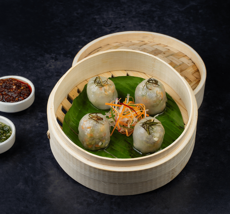 Vegetable Cristal Dumpling placed on a basket and next to it there are two types of dips served in a small bowl at  The Wild Fork restaurant in La Marvella, Bengaluru. 