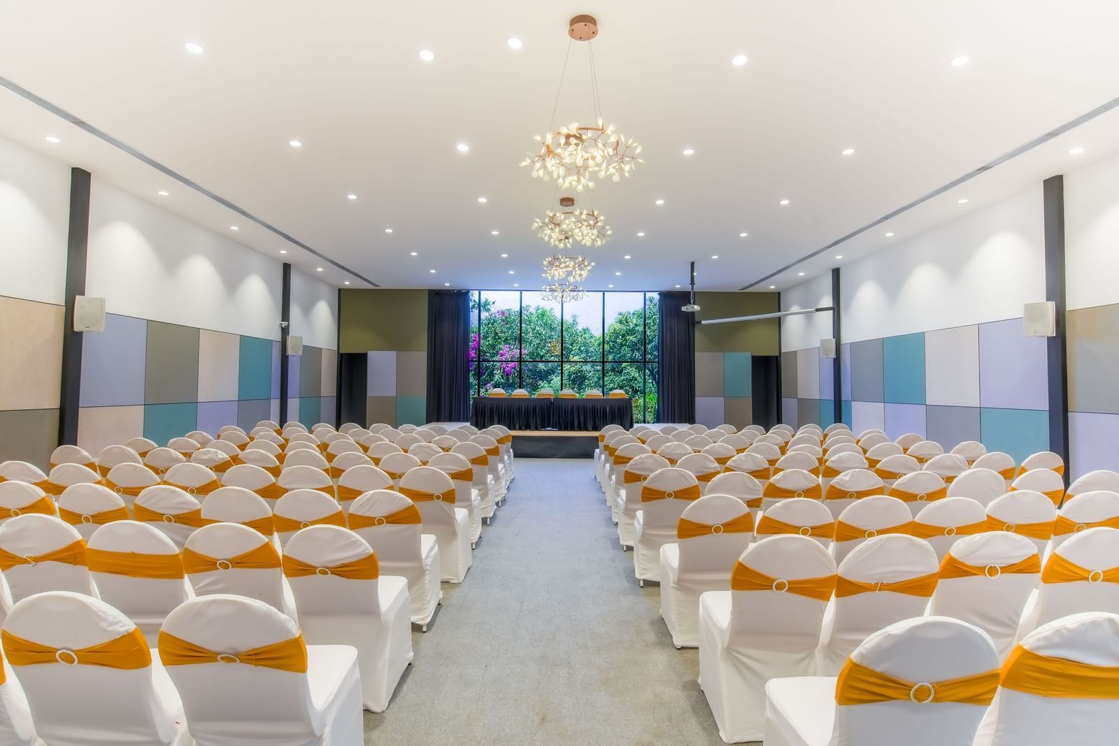 Interior of Royal Affair at Darza Resort featuring a large, brightly lit conference hall is set up with rows of white chairs adorned with gold sashes, facing a stage area.