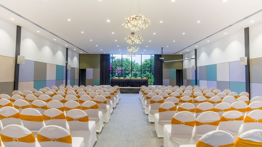 Interior of Royal Affair at Darza Resort featuring a large, brightly lit conference hall is set up with rows of white chairs adorned with gold sashes, facing a stage area.