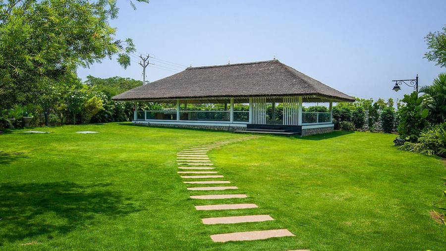 Slice of Heaven at Darza Resort featuring stone pathway meandering across a bright green lawn towards a white, open-sided structure with a dark roof, set under a clear blue sky.