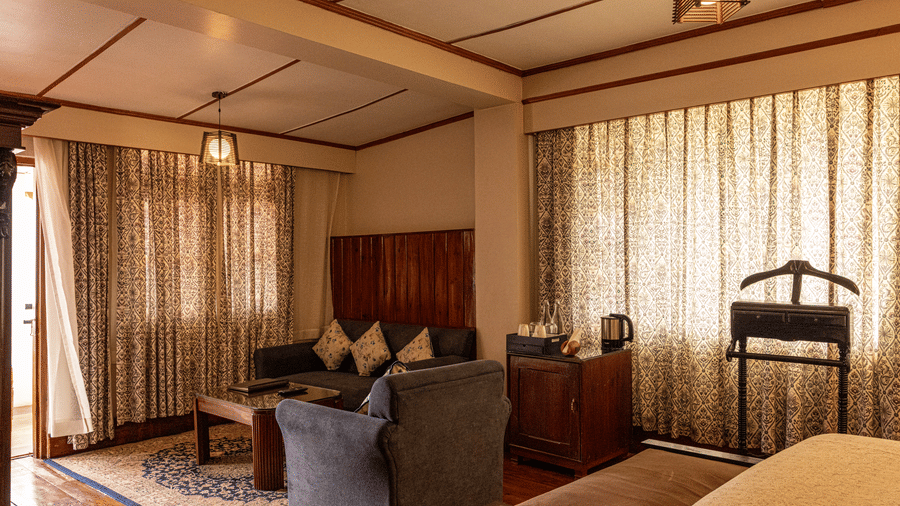 A room at The Heritage Club, Tripura, Castle, Shillong, featuring tables, sofas, and a large window covered with curtains.
