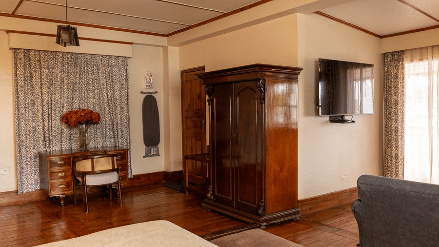 A room at The Heritage Club, Tripura, Castle, Shillong, featuring a flower vase placed on a table, sofas, a television, and a  wardrobe.