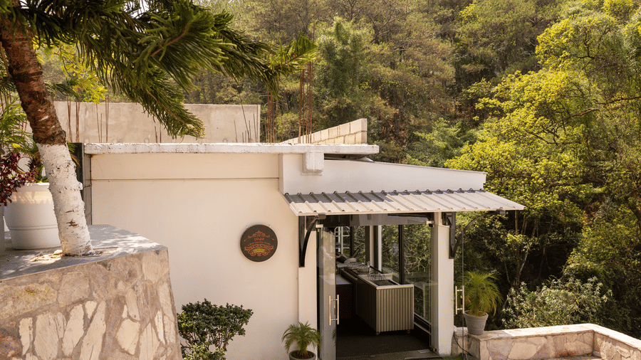 A dining facade structure nestled against a densely forested. | The Heritage Club, Tripura, Castle, Shillong