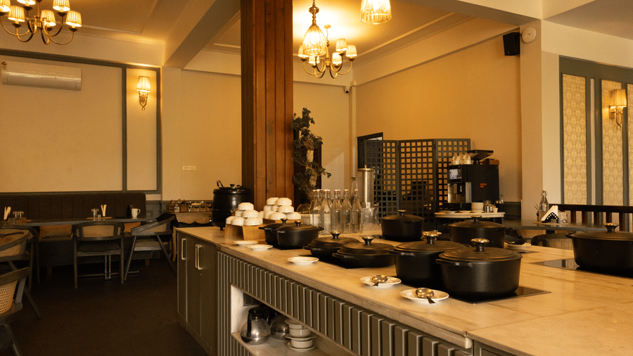 A dining space at The Heritage Club, Tripura Castle, Shillong, with lamps, tables, chairs, and vessels placed on a shelf. 
