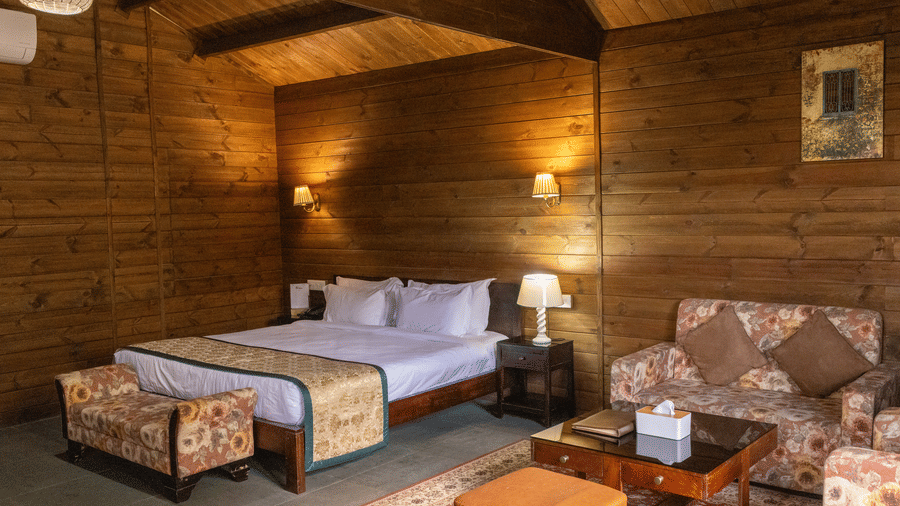 A room at The Heritage Club, Tripura, Castle, Shillong, featuring a large bed, pillows, spreads, cushions, and a small table.