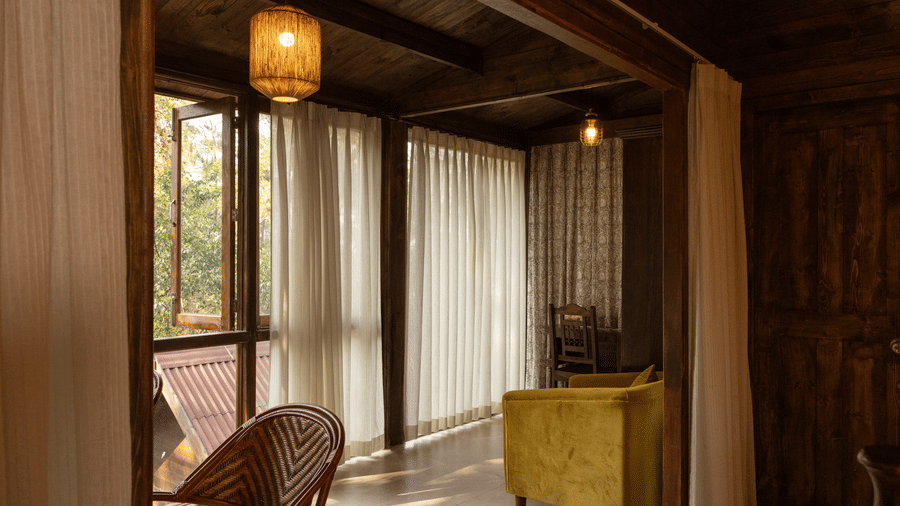 A room at The Heritage Club, Tripura, Castle, Shillong, featuring a chair, a table, and wooden window.