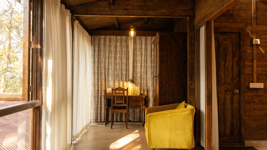 A room at The Heritage Club, Tripura, Castle, Shillong, featuring a cushion, chairs, a chandelier, and a windows covered with curtains.