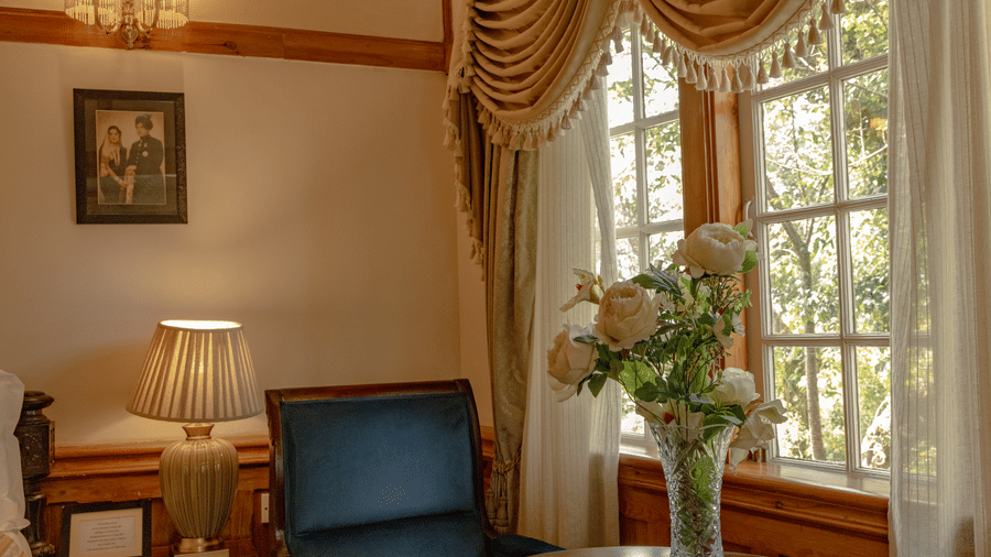 A room at The Heritage Club, Tripura, Castle, Shillong, showcasing a window, tables, lamps, a sofa, and a flower vase.