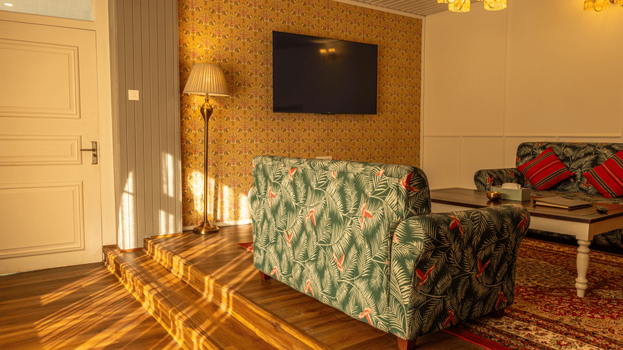 A room at The Heritage Club, Tripura, Castle, Shillong, featuring sofas, a television, and stairs.