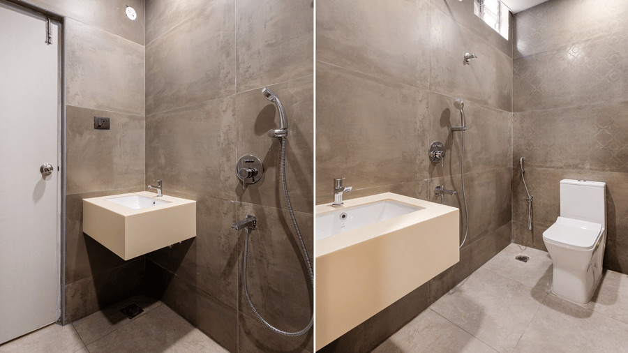 A bathroom split view displaying a sink counter, shower fixture, and flush toilet against grey tiled walls at Monday Hotels & Suites Madhapur Hyderabad.