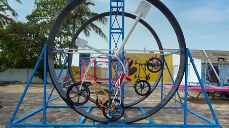 A large, colourful playground structure at MGM Dizzee World featuring a big Ferris wheel-like contraption and other climbing elements, on a sandy ground.