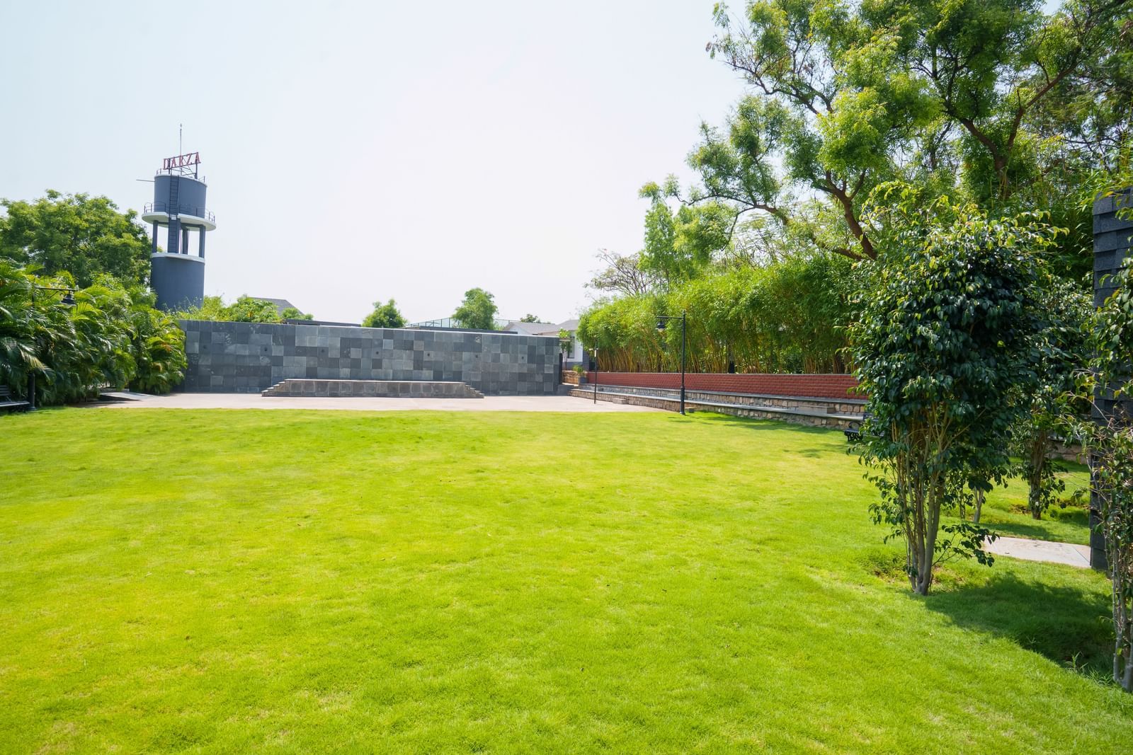 Enchante at Darza Resort featuring a wide expanse of bright green lawn is surrounded by trees, hedges, and a stone wall, with a tower visible in the distance under a clear sky.