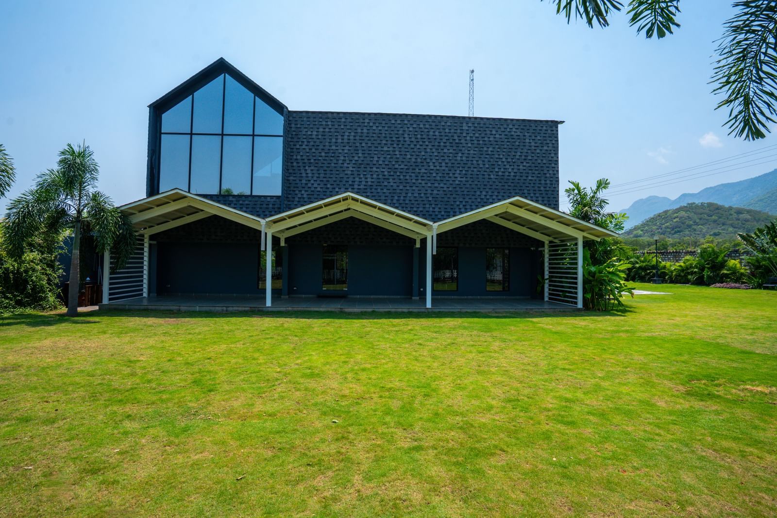 Love Letter at Darza Resort featuring a modern, dark-coloured building with large windows and covered porches sits on a bright green lawn under a clear, sunny sky.