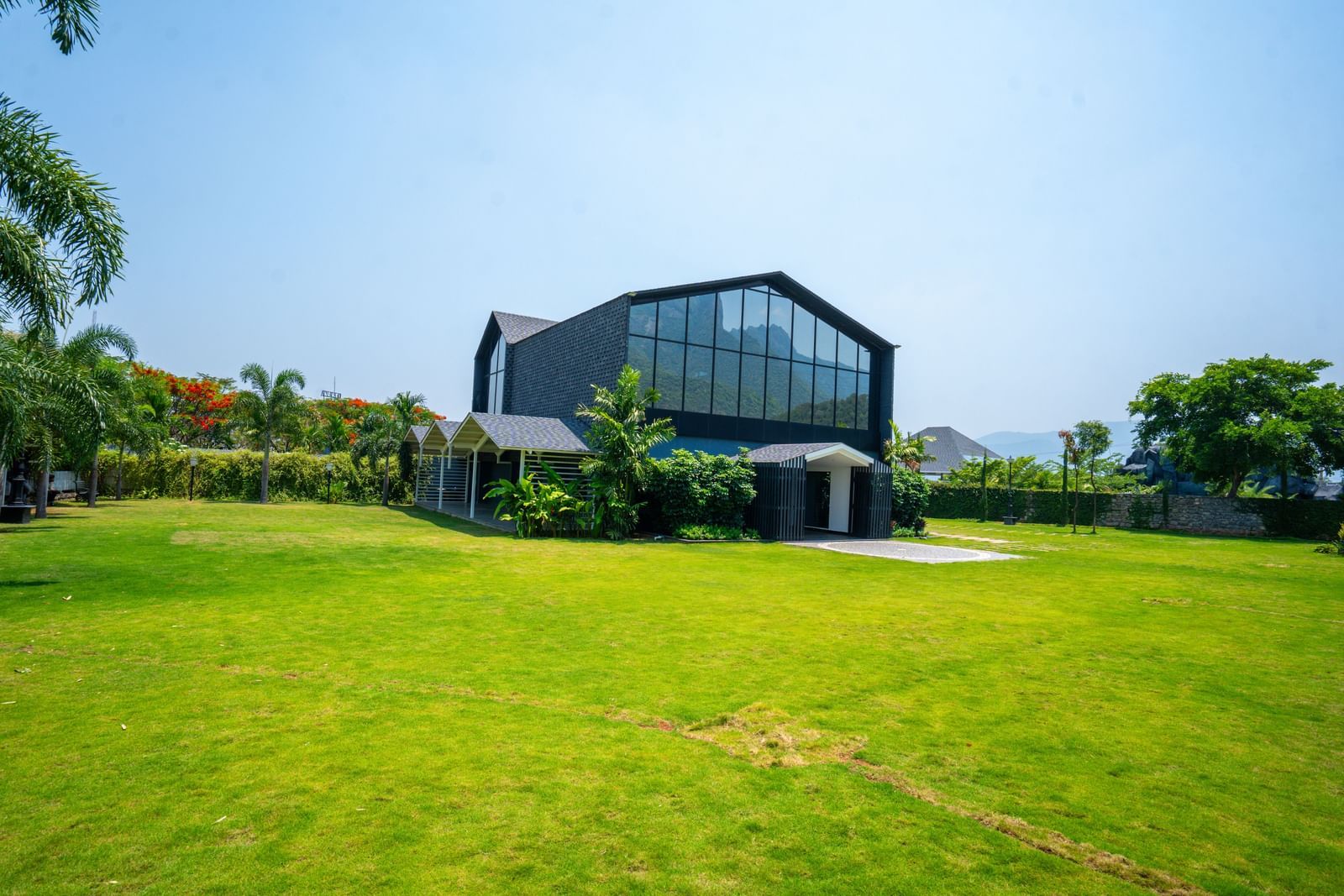 Facade of Love Letter at Darza Resort with large windows standing on a sprawling green lawn under a bright blue sky, surrounded by greenery.
