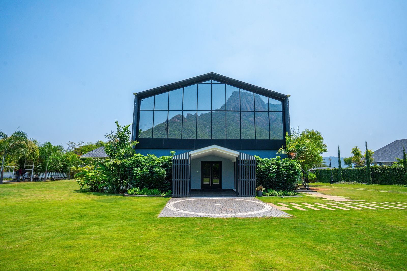 Entrance of Love Letter at Darza Resort with large glass windows reflecting the sky stands on a vibrant green lawn surrounded by greenery.