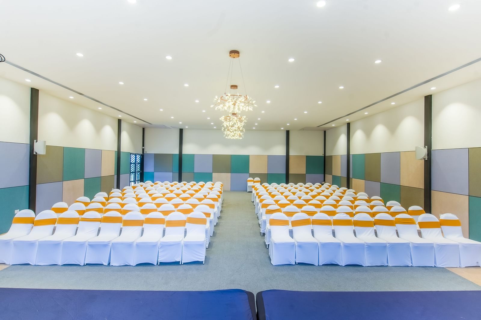 A well-lit Royal Affair at Darza Resort is arranged with numerous white chairs decorated with orange sashes, set up for an audience facing a stage area.