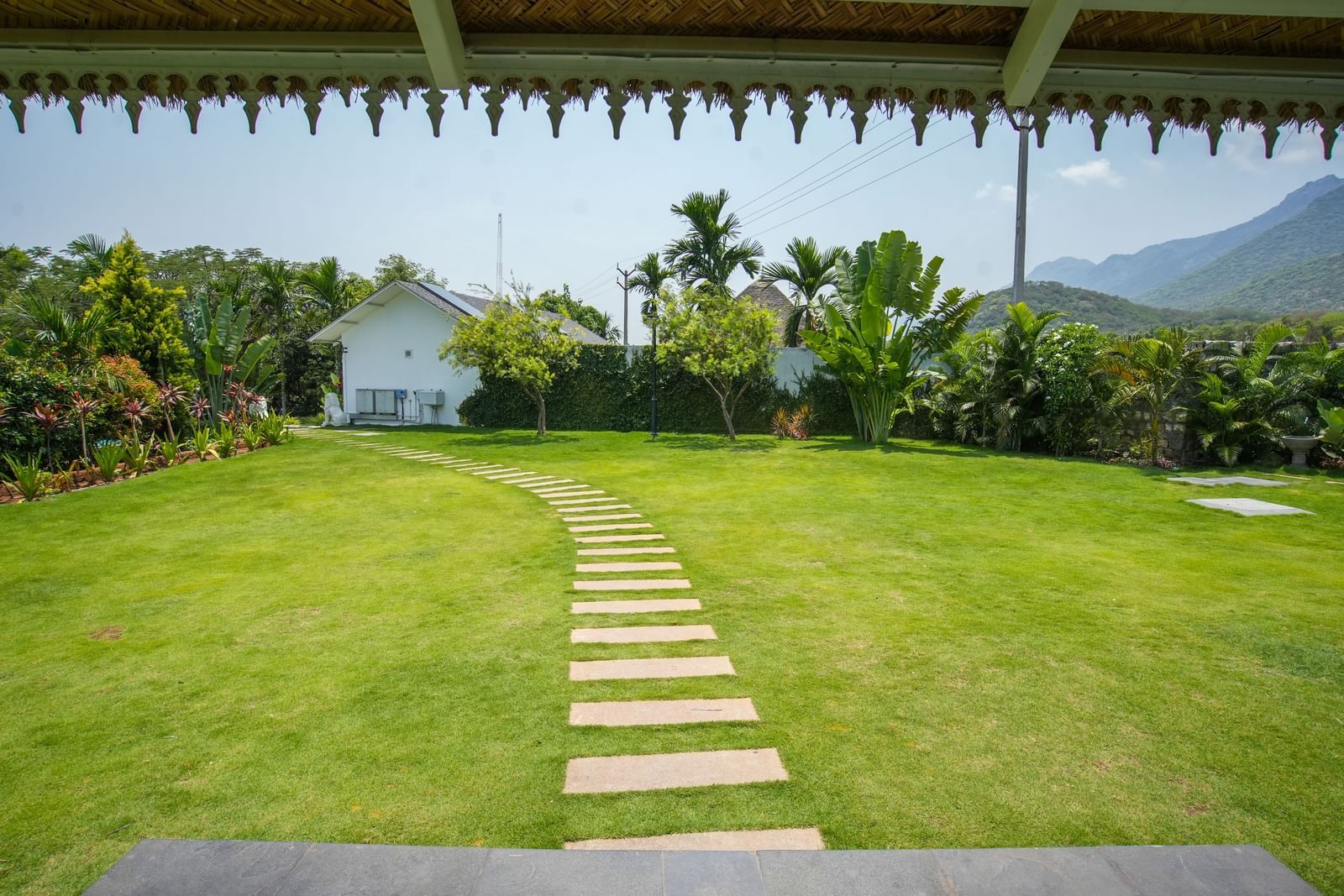 Slice of Heaven at Darza Resort featuring a stone pathway winding through a lush green lawn, leading towards white buildings and tropical foliage under a bright, clear sky.
