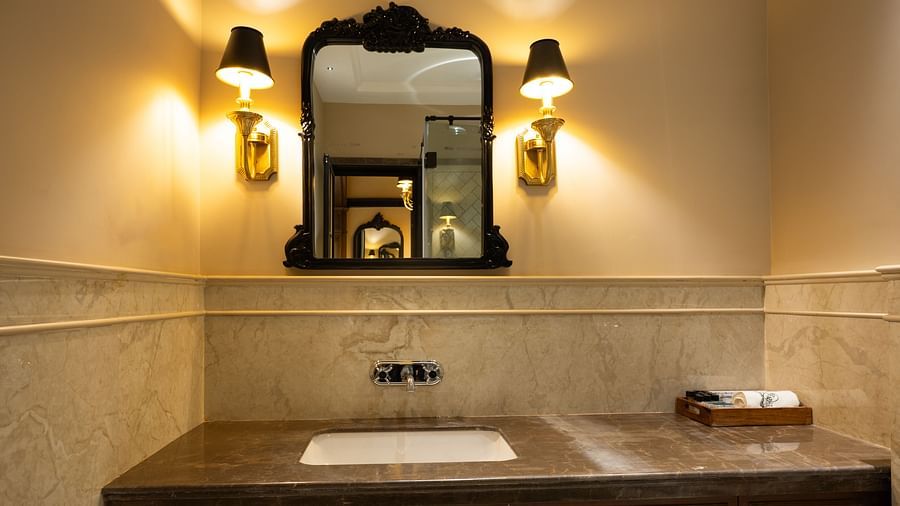 Bathroom vanity with a dark framed mirror, wall-mounted lamps on both sides, and a countertop with a built-in sink and toiletry tray - Panna Vilas Palace