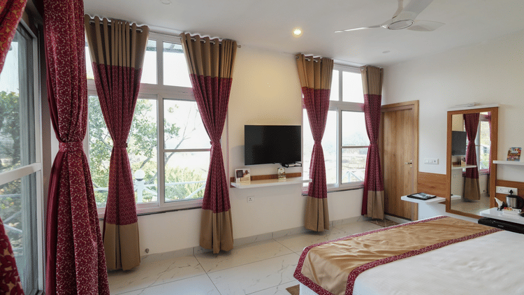 a bedroom with a bed facing a mounted television with windows on both sides of it- MGM Whispering Wind's, Yelagiri