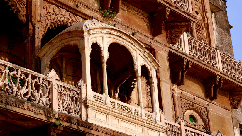 An ornate stone balcony with detailed carved arches and delicate railings projects from the weathered wall of Ramnagar Fort in Varanasi.