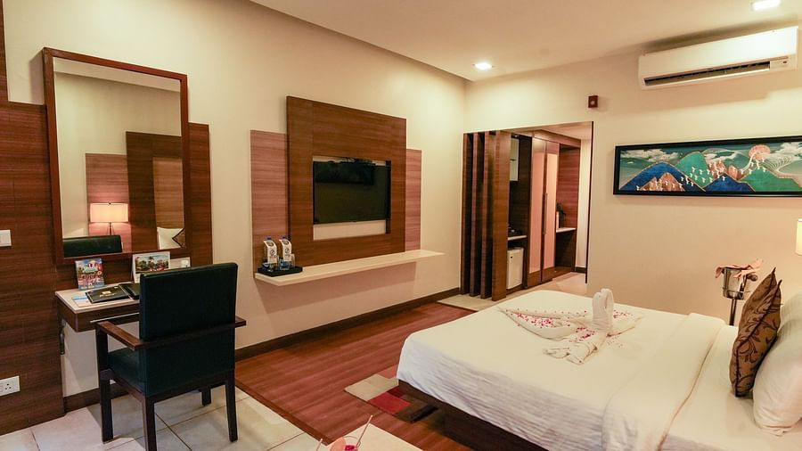 A hotel room with a bed, a dressing table with a chair, a wall-mounted TV, and cupboards
