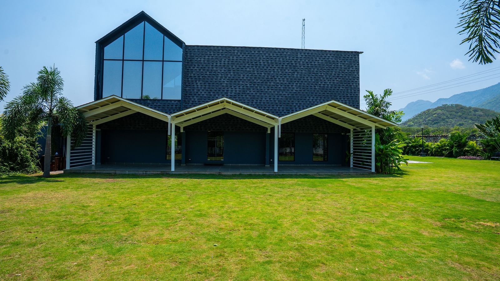 Love Letter at Darza Resort featuring a modern, dark-coloured building with large windows and covered porches sits on a bright green lawn under a clear, sunny sky.