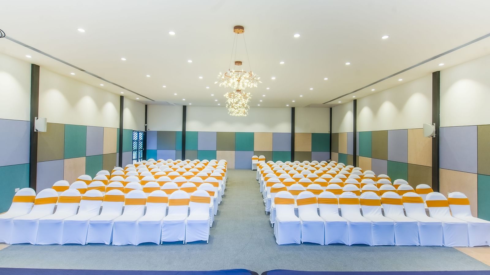 A well-lit Royal Affair at Darza Resort is arranged with numerous white chairs decorated with orange sashes, set up for an audience facing a stage area.
