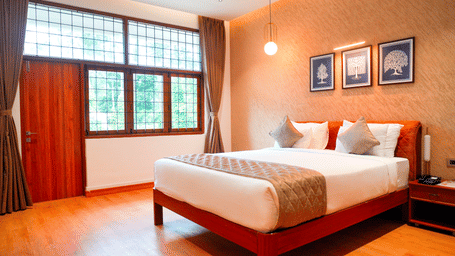 A bedroom with a bed, curtains, and wall frames at DNC Shevaroys Resorts and Spa.