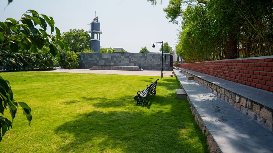 Enchante at Darza Resort featuring a bright green lawn, bordered by trees and a brick wall, features a bench and a distant tower under a sunny sky.